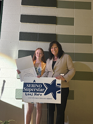 Sue Serino taking picture with honoree with certificate and yard sign